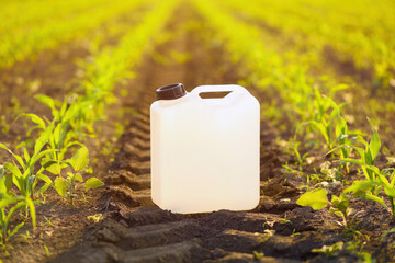 Blank white herbicide canister can in corn seedling field in springtime sunset
