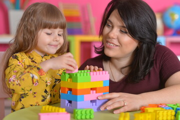 Little girl and mother playing with colorful plastic blocks