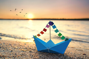 Fototapeta na wymiar Papierschiffchen mit bunten Segel am Strand