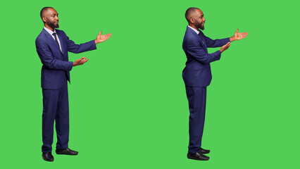 Young businessman creating presentation in studio, talking about something on left or right sides. Male office employee doing advertisement over full body green screen background. © DC Studio