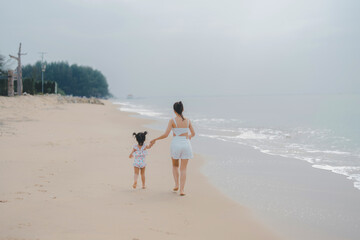 Fototapeta na wymiar back side view happy time of mom and daughter in dress white walking and run play on the beach morning time with blur background