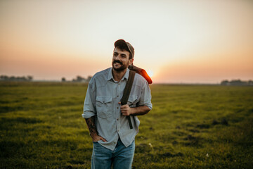 Caucasian man backpacker hiking outdoors during sunset. Handsome guy enjoys an adventurous outdoor lifestyle walking on a grassy dirt road on summer vacation. Ecotourism and solo travel concept.