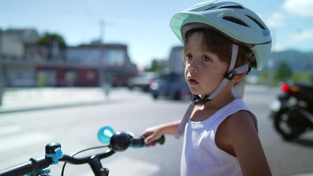 Child standing in street waiting to cross holding bicycle. One small boy wearing helmet in standby at pedestrian red light at crosswalk