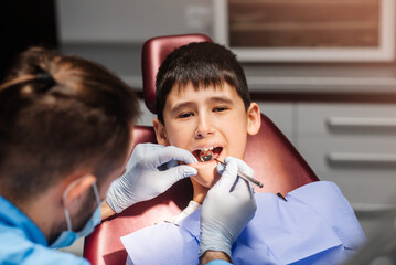 Masked dentist examining little boy's teeth in clinic. Pediatric dentistry. The dentist examines the patient's mouth.