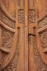 Vintage wooden door with carvings of flowers and plants painted with old brown paint.