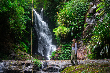 hiker girl stands gazing at an amazing tropical waterfall (elabana falls) in lamington national...