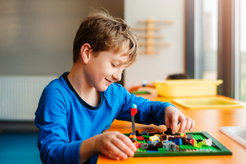 Little boy playing with plastic brick children's constructor at kindergarten.