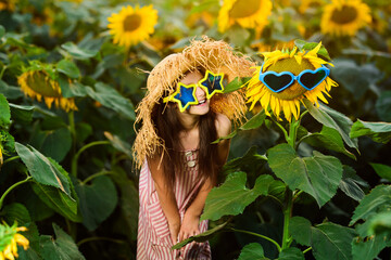 Little pretty girl posing among a field of sunflowers. Trendy summer children's hats and clothes....