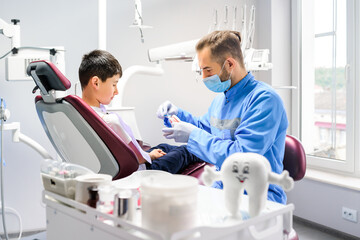 Male masked dentist showing on a jaw model how to clean the teeth.