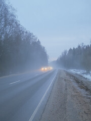 Blurred image of cars with headlights on driving on a country road in the fog.