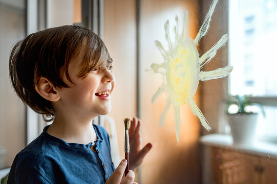 Happy boy with paintbrush drawing sun on glass