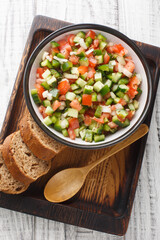 Vegetable salad with tomatoes, green peppers, onions and cucumbers close-up in a bowl on a wooden board. Vertical top view from above