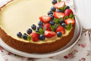Whole round new york cheesecake with strawberries, blueberries and mint close-up on a plate on the table. Horizontal