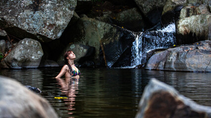 a beautiful girl in a bikini takes a refreshing swim at a waterfall at cedar creek swimming holes...