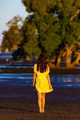 girl wearing yellow dress admires colourful sunset wading in the shallow water at nudgee beach, brisbane, queensland, australia; mangroves in boondall wetlands