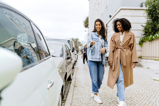Happy woman with friend unlocking car with remote key