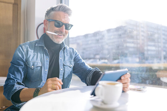 Smiling mature businessman with digitized pen using tablet PC in cafe - Powered by Adobe