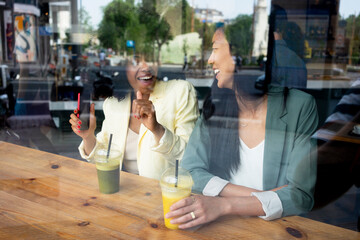 Happy woman talking to friend sitting with juice in cafe seen through window