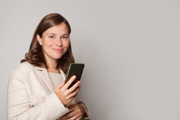 Fototapeta premium Young pregnant woman using her mobile phone to send message against white studio wall background