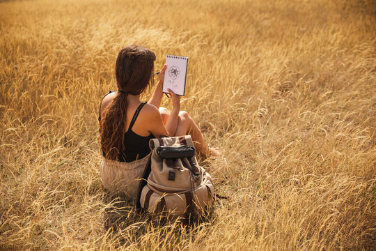 Young woman sitting on dry grass looking at flower drawing