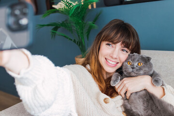 Happy woman taking selfie with cat through smart phone at home