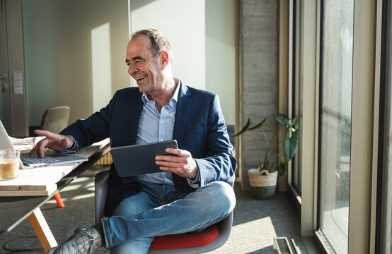 Happy businessman using laptop and holding tablet PC in office