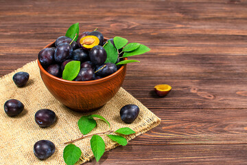 Blue plum in a bowl on a wooden table. Plums in the cut. Place for text. Fruit background with copy space.
