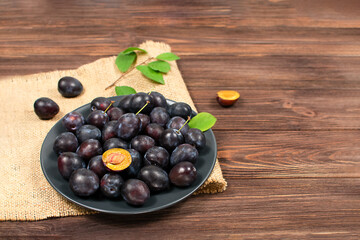 Blue plum in a plate on a wooden table. Place for text. Fruit background with copy space.