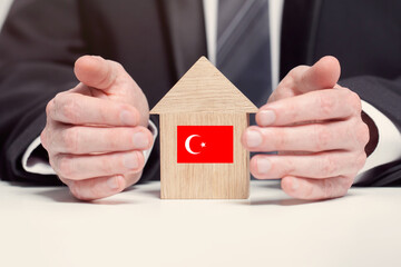 Businessman hand holding wooden home model with Turkish flag. insurance and property concepts