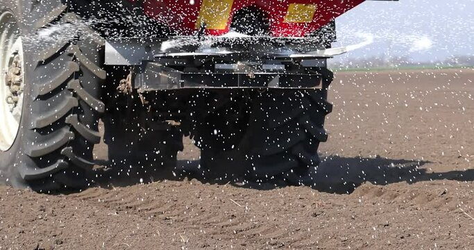 Farmer with agricultural machinery fertilizing agricultural field in spring time, slow motion. Spreading mineral fertilizer, cinematic low angle gimbal shot