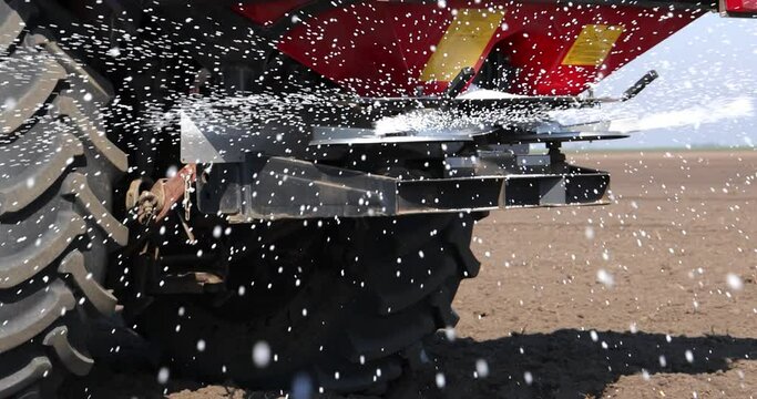Farmer with agricultural machinery fertilizing agricultural field in spring time, slow motion. Spreading mineral fertilizer, low angle shot