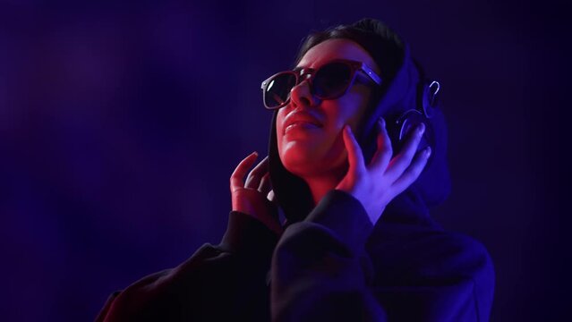 Trendy teenager woman headphones listening music audio sound disco dark neon light closeup