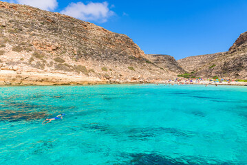 Cala Pulcino in Lampedusa seen from a boat. Stunning turquoise sea water in a secluded bay surrounded by cliffs. Sicily, Italy.