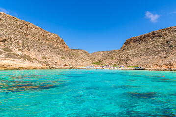 Fototapeta na wymiar Cala Pulcino in Lampedusa seen from a boat. Stunning turquoise sea water in a secluded bay surrounded by cliffs. Sicily, Italy.