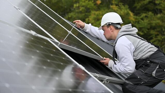 Man technician mounting photovoltaic solar panels on roof of house. Engineer in helmet installing solar module system with help of hex key. Concept of alternative, renewable energy.