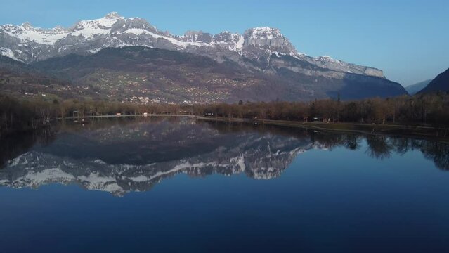 Sallanches, France below the snow-capped mountains reflected in the water of Passy Lake - aerial flyover
