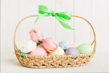 Happy Easter composition. Easter eggs in basket on colored table with yellow Tulips. Natural dyed colorful eggs background with copy space