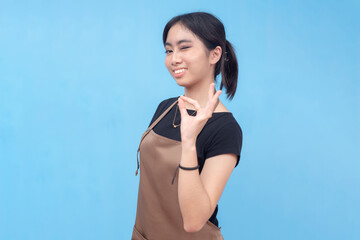 A young and confident asian female waitress or barista winks while making the ok sign. Wearing a...
