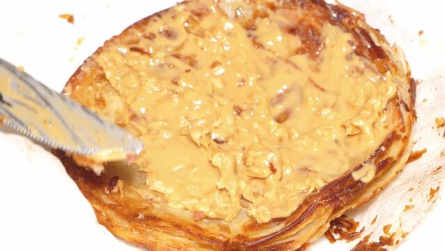 Slow motion speed close up scene on knife spread peanut butter on roti isolated on white paper background, sandwich bread making for some meal tasty menu, unhealthy fast food appetize