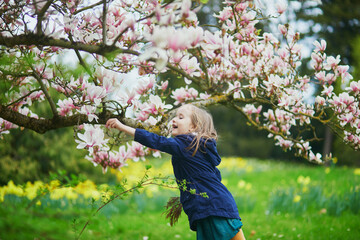 Adorable preschooler girl enjoying nice spring day in park during magnolia blooming season