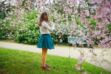 Adorable preschooler girl enjoying nice spring day in park during cherry blossom season