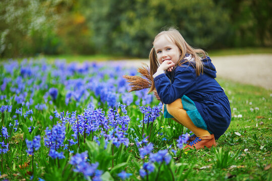 Adorable preschooler girl enjoying nice spring day in park during hyacinth blooming season