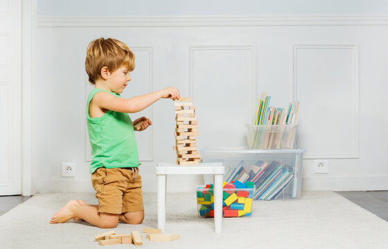 Boy build Jenga tower of wooden blocks on the carpet in a room