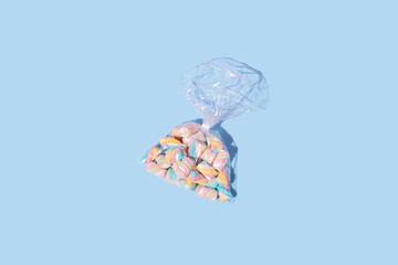 Marshmallow candies in wrapped transparent plastic bag on pastel blue background. Sweet food concept.