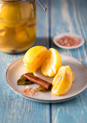 Pickled lemons with bay leaf on white plate and fresh salt. Blue wood background.
