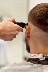 Obraz na płótnie Canvas Barber trim hair with clipper on handsome bearded man
