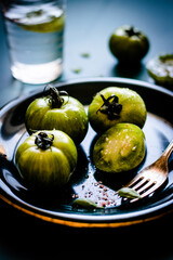 Fresh green tomatoes with salt and glass of water on dark blue plate. Back light