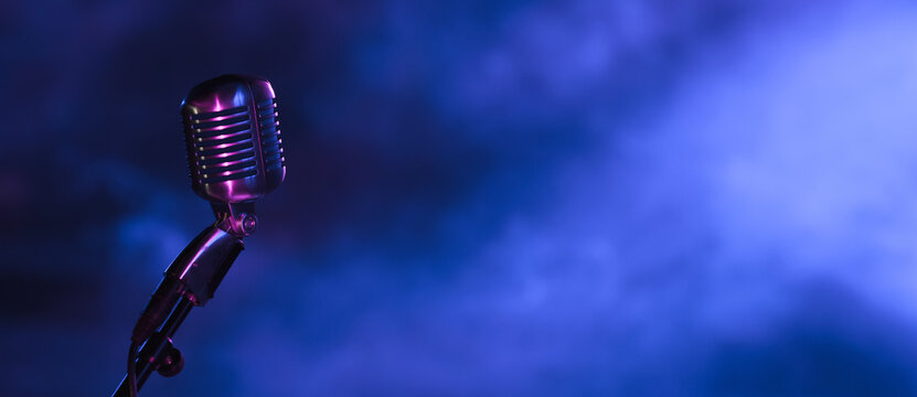 retro microphone in the dark with blue light from stage spotlights. Vintage mic on dark blue background for music live, music festival, karaoke or podcast banner with copy space.