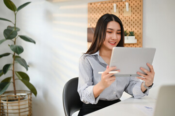 Attractive Asian businesswoman using her digital tablet at her desk in her office.