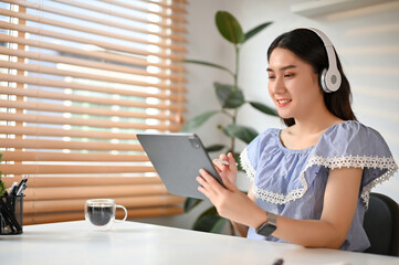 Happy Asian woman using her tablet and listening to music through her headphones